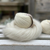 A swirl of natural cream coloured yarn with two balls of natural cream coloured yarn