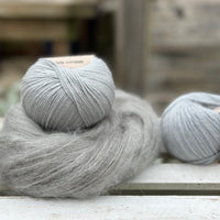 A swirl of fluffy grey yarn alongside 2 balls of pale blue yarn