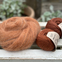 A swirl of fluffy reddish-brown yarn with two balls of reddish-brown yarn