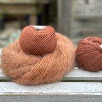 A swirl of fluffy reddish-brown yarn with two balls of reddish-brown yarn