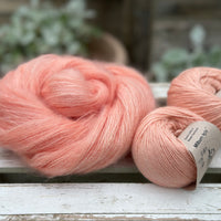 A swirl of fluffy pink yarn with two balls of peachy orange yarn