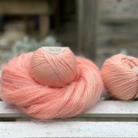 A swirl of fluffy pink yarn with two balls of peachy orange yarn