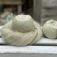 A swirl of fluffy green yarn with two balls of pale green yarn