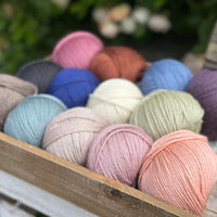 A wooden tray containing 13 balls of yarn in the colours selected to use in the Spirit of Flora pattern