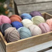 A wooden tray containing 13 balls of yarn in the colours selected to use in the Spirit of Flora pattern