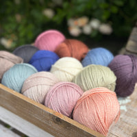 A wooden tray containing 13 balls of yarn in the colours selected to use in the Spirit of Flora pattern