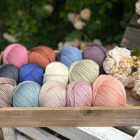 A wooden tray containing 13 balls of yarn in the colours selected to use in the Spirit of Flora pattern