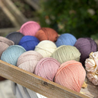 A wooden tray containing 13 balls of yarn in the colours selected to use in the Spirit of Flora pattern