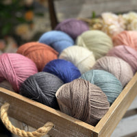 A wooden tray containing 13 balls of yarn in the colours selected to use in the Spirit of Flora pattern