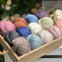 A wooden tray containing 13 balls of yarn in the colours selected to use in the Spirit of Flora pattern