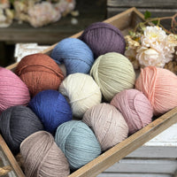 A wooden tray containing 13 balls of yarn in the colours selected to use in the Spirit of Flora pattern