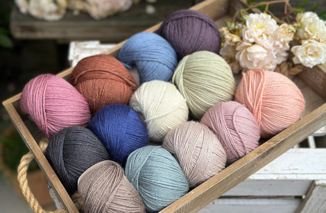 A wooden tray containing 13 balls of yarn in the colours selected to use in the Spirit of Flora pattern