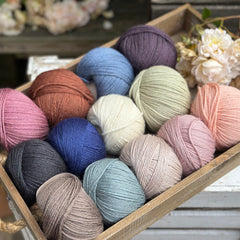 A wooden tray containing 13 balls of yarn in the colours selected to use in the Spirit of Flora pattern