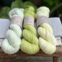 three different skeins of hand dyed yarn in semi solid shades, which are very pale green, light lime green, and very light yellow. 