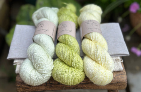 three different skeins of hand dyed yarn in semi solid shades, which are very pale green, light lime green, and very light yellow. 