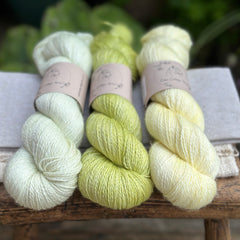 three different skeins of hand dyed yarn in semi solid shades, which are very pale green, light lime green, and very light yellow. 