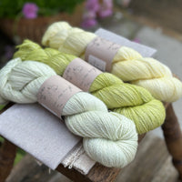 three different skeins of hand dyed yarn in semi solid shades, which are very pale green, light lime green, and very light yellow. 