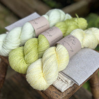 three different skeins of hand dyed yarn in semi solid shades, which are very pale green, light lime green, and very light yellow. 