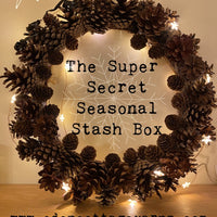 A wreath of pine cones and fairy lights, with text in the centre saying The Super Secret Seasonal Stash Box, and text below saying www.ededncottageyarns.com