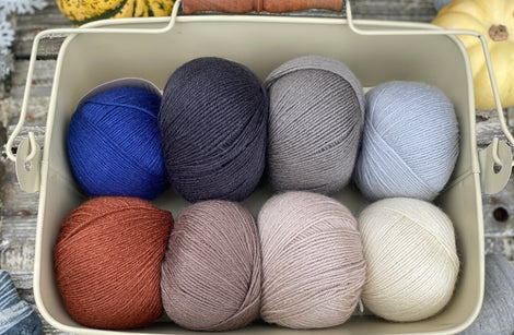 Eight balls of Milburn 4ply in shades of brown and grey with pops of red and blue