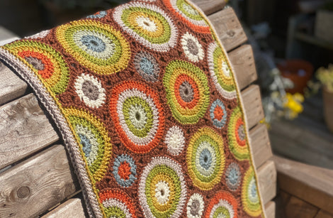 A crocheted rectangular wrap which has an all-over motif of multicoloured circles.